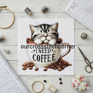 Op de afbeelding: Kruissteekontwerp met een grijs-witte kat in een koffiekopje. Op het kopje staat "I NEED COFFEE", omringd door koffiebonen. Naaibenodigdheden zoals garenklosjes en een schaar zijn ook zichtbaar.