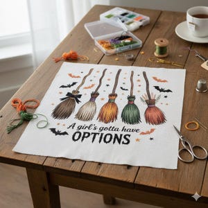 Può includere: Un progetto a punto croce bianco con la frase "A girl's gotta have OPTIONS" e illustrazioni di cinque colorate scope da strega. Le scope sono marroni, nere, arancioni, verdi e rosse. Sono inclusi anche pipistrelli e stelle. Materiali da cucito sul tavolo di legno.