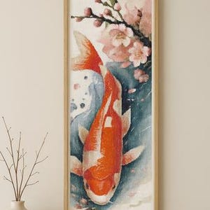 May include: Framed artwork featuring a vibrant orange and white koi fish swimming in blue water, with pink cherry blossoms in the background. The rectangular frame is made of light-colored wood. The artwork is a vertical rectangle.