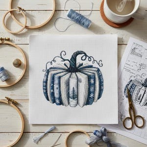 May include: Cross-stitch design of a pumpkin made of books, featuring blue and white colors. The pumpkin has a dark blue stem and is surrounded by embroidery hoops, thread, and a cup of tea.