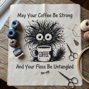 以下が含まれることがあります： 「May Your Coffee Be Strong And Your Floss Be Untangled」のテキストが入ったクロスステッチプロジェクト。コーヒーカップを持った黒い生き物を描いています。刺繍糸、ハサミ、刺繍枠が含まれています。