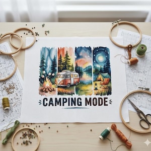 May include: A cross-stitch design depicting a camping scene with a vintage camper van, campfire, and lake. The text "CAMPING MODE" is below the image. Embroidery hoops, thread, and scissors are arranged around the project.