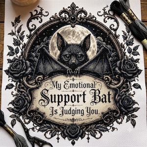 Könnte beinhalten: Ein Kreuzstichmuster auf weißem Stoff mit einer schwarzen Fledermaus vor einem Vollmond, umrahmt von dunklen Rosen und kunstvollen Verzierungen. Der Text lautet, My Emotional Support Bat Is Judging You. Schwarzes Stickgarn und eine Schere.