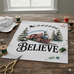 May include: A cross-stitch project featuring a red train with the word "BELIEVE" in black script. The design includes Santa's sleigh and reindeer, pine trees, and steam. Sewing supplies like thread spools, scissors, and needles are scattered around the project.