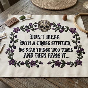 May include: A cross-stitch project with the text "DON'T MESS WITH A CROSS STITCHER. WE STAB THINGS 1000 TIMES AND THEN HANG IT..." surrounded by a floral and skull design. The image includes embroidery supplies like scissors, thread, and a wooden hoop.
