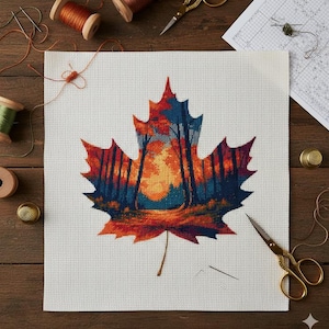 May include: A cross-stitch project featuring a colorful autumn leaf design. The leaf is filled with a forest scene in shades of orange, red, and blue. The project is on white fabric, with spools of thread, scissors, and thimbles on a wooden surface.