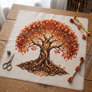 May include: A cross-stitch project on beige fabric featuring a large tree with intricate brown roots and vibrant orange, red, and yellow autumn leaves. Included are metal scissors, a thimble, three embroidery floss skeins, and a clear ruler.