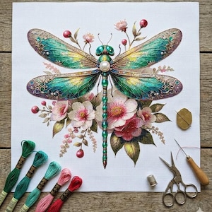May include: Cross-stitch design of a dragonfly with iridescent green and blue wings, pearl accents, and a beaded body. The dragonfly is surrounded by pink and red flowers. Embroidery floss, scissors, and other tools are visible.