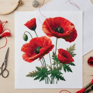 May include: A completed cross-stitch project featuring vibrant red poppy flowers with dark green leaves and black centers. The needlework is on white fabric, with embroidery supplies like scissors, thread, and a hoop visible.