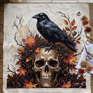 May include: A cross-stitch embroidery project on white fabric featuring a black raven perched atop a human skull. The design is surrounded by autumn leaves, pinecones, and berries in shades of orange, red, and brown, with gold swirl accents.