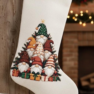 May include: A cream-coloured Christmas stocking with a gnome design. The stocking features a group of gnomes wearing colourful hats and holding gifts. The gnomes are surrounded by green pine needles. The stocking hangs on a wooden surface.