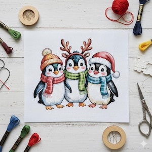 May include: Cross-stitch of three penguins wearing winter hats and scarves. The penguins are decorated with a reindeer antler headband, a Santa hat, and a knit cap. The penguins are on a white background with embroidery supplies.