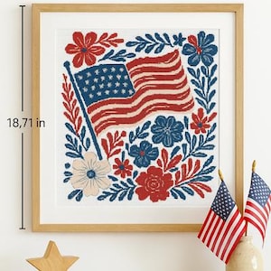 Könnte beinhalten: Gerahmtes Kunstwerk mit einem patriotischen Design, das eine amerikanische Flagge und florale Elemente zeigt. Das Kunstwerk ist 40,3 cm breit und 47,5 cm hoch. Zwei kleine amerikanische Flaggen und ein Holzstern stehen auf einer Holzoberfläche.