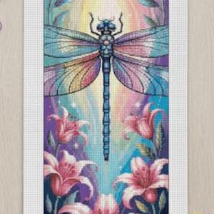 May include: A cross-stitch pattern featuring a dragonfly with colorful wings and a blue body, set against a backdrop of pink lilies and a rainbow-colored sky. The artwork is framed with a white border and surrounded by craft supplies.
