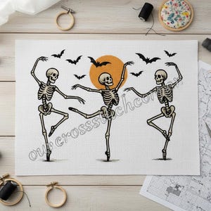 Peut inclure: Motif de point de croix représentant trois squelettes dansant le ballet, avec un soleil jaune et des chauves-souris noires. Le motif est sur tissu blanc, idéal pour Halloween.