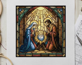 May include: A cross-stitch design depicting the Nativity scene in a stained-glass style. The image features Mary and Joseph kneeling beside the baby Jesus in a manger, with a radiant sunburst background. The color palette includes blues, reds, and golds.
