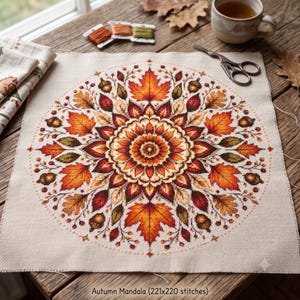 May include: A cross-stitch embroidery project on beige fabric featuring a circular mandala design composed of autumn leaves, acorns, and berries in shades of orange, red, yellow, and brown. The text at the bottom reads Autumn Mandala (221x220 stitches).