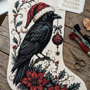 Puede incluir: Un calcetín navideño de punto de cruz con un cuervo negro que lleva un gorro de Papá Noel rojo y sostiene un adorno rojo y negro en el pico. El diseño incluye ramas de acebo, bayas rojas y flores de pascua. Una etiqueta dice Flipped Pattern Included.