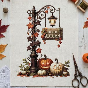 May include: Cross-stitch design featuring a vintage lamppost with a sign that reads "Hello Autumn." The scene includes carved pumpkins, fall foliage, and a lit lantern. The design is on a cream-colored fabric, with spools of thread and scissors nearby.