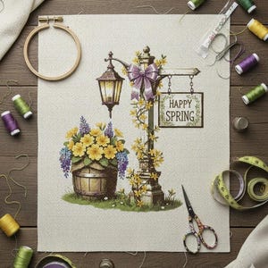 May include: Cross-stitch embroidery of a street lamp with a sign that reads "Happy Spring". The lamp is decorated with a purple bow and yellow flowers. A wooden barrel filled with yellow and purple flowers is in front of the lamp.