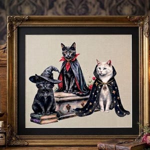 Może przedstawiać: Oprawione dzieło sztuki przedstawiające trzy koty w kostiumach na Halloween. Jeden kot ma na sobie kapelusz czarownicy, drugi pelerynę wampira, a trzeci płaszcz w gwiazdy. Dzieło jest w złotej ramie, z świecami i dekoracjami w tle.