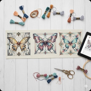 May include: A cross-stitch project featuring three butterfly designs in shades of gold, pink, and blue. Various spools of embroidery floss in coordinating colors, scissors, and a tablet with a digital pattern are also present. A wooden embroidery hoop is also visible.