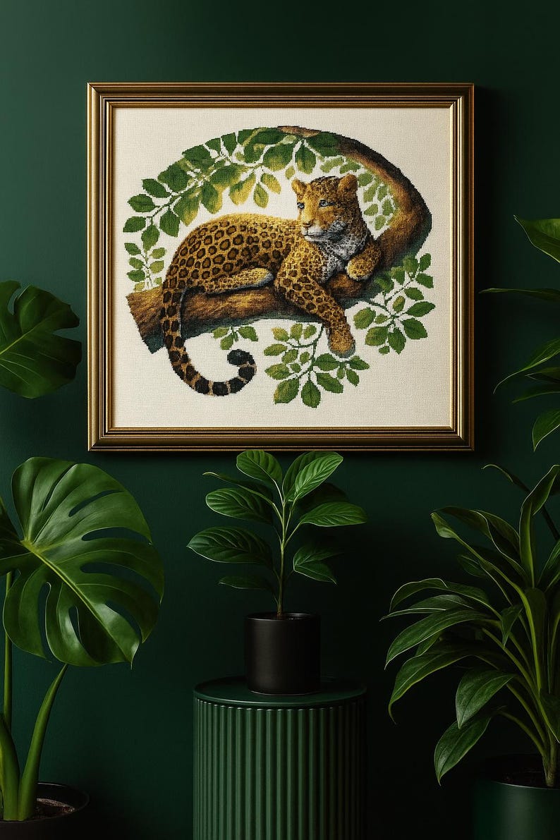 May include: A framed artwork featuring a leopard resting on a tree branch, surrounded by green leaves. The leopard has a tan coat with dark spots. The frame is gold-colored, and the background is a dark green. Potted plants are in the foreground.