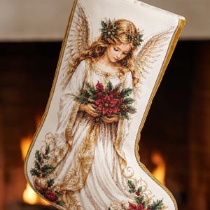 May include: A cream-colored Christmas stocking featuring a detailed needlepoint design of an angel with large wings, wearing a white gown and a holly wreath, holding a bouquet of red poinsettias, finished with gold braided trim and a hanging loop.