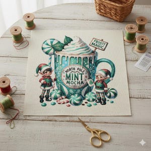 Puede incluir: Un diseño de punto de cruz con una taza festiva de North Pole Mint Mocha con crema batida, elfos y caramelos. El diseño incluye el texto "Frosty Magic" y "North Pole Mint Mocha". La paleta de colores incluye verde azulado, rojo y blanco.