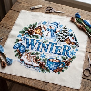 May include: A square piece of fabric featuring a cross-stitch design with the word WINTER in large blue letters. The embroidery includes a snowman, ice skates, a mug of cocoa, pine trees, a lantern, and snowflakes in blue and white.