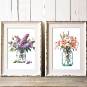 Pode incluir: Duas impressões em aquarela emolduradas. Uma apresenta lilases roxos em um frasco de vidro, a outra mostra lírios rosa em um frasco semelhante. Ambas estão em um fundo branco, com molduras brancas desgastadas, em uma superfície de madeira.