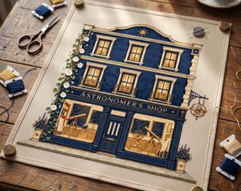 May include: A cross-stitch embroidery piece on a light fabric background depicting a three-story building labeled ASTRONOMER'S SHOP. The facade is dark blue with gold-toned windows, a telescope in the storefront, and climbing white flowers.