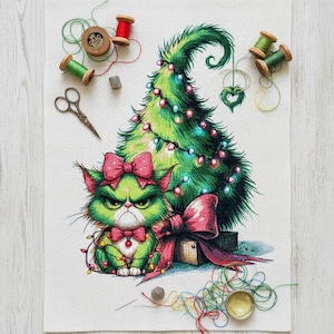 May include: Cross-stitch design of a grumpy green cat with a pink bow, beside a decorated Christmas tree. The image includes spools of thread, scissors, and a needle, indicating a crafting theme.