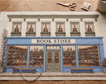 May include: A needlepoint canvas depicting a bookstore facade with a blue storefront, large display windows showing interior bookshelves, and the text BOOK STORE. The design includes a climbing plant, two benches, and upper-story windows with flower boxes.
