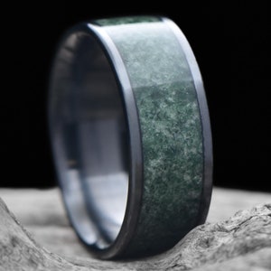 May include: A dark gray and green ring with a textured green band. The ring is made of tungsten carbide and has a polished finish.
