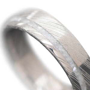 May include: A silver wedding band with a hammered finish and a row of small white diamonds.