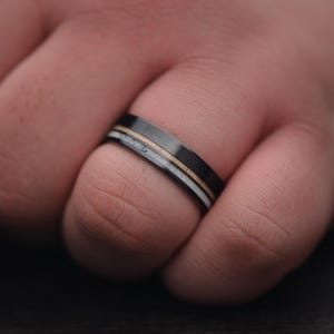Mens black titanium wedding band with deer antler and birds eye maple inlays, 7mm polished flat profile, shown on a hand, free engraving available.