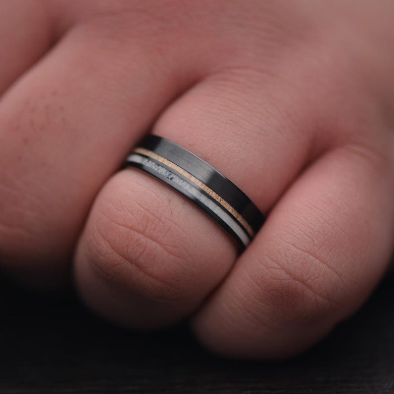Mens black titanium wedding band with deer antler and birds eye maple inlays, 7mm polished flat profile, shown on a hand, free engraving available.
