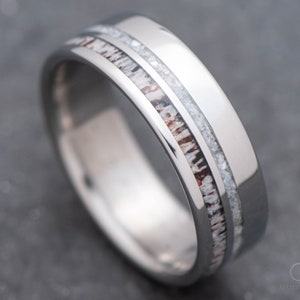 May include: A silver titanium ring with a brown and white inlay. The inlay is a thin strip of wood with a white stripe running down the center.