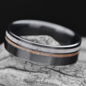Black titanium wedding band with deer antler and birds eye maple inlays, featuring free engraving, 7mm width, mens polished flat profile ring, displayed on a white sea branch., 8995
