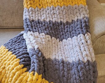 May include: A chunky knit throw blanket with a chevron pattern in shades of mustard yellow, gray, and white.