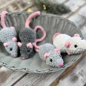 May include: Four crocheted plush mice in a wicker basket. Three are gray with pink ears and noses, and one is white with pink ears and nose.