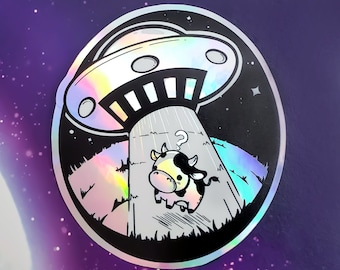 Puede incluir: Una pegatina en blanco y negro con un acabado holográfico. La pegatina presenta una vaca de dibujos animados con un signo de interrogación sobre su cabeza, de pie frente a un OVNI. El OVNI está flotando sobre un campo de hierba.