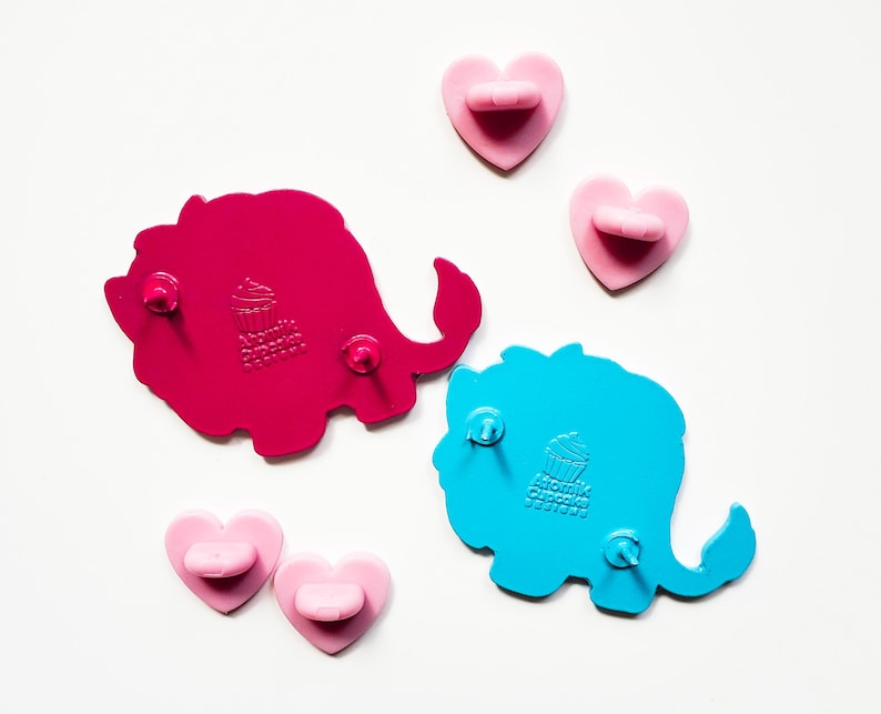 K&ouml;nnte beinhalten: Zwei Elefanten-f&ouml;rmige Anstecknadeln aus Emaille. Der rosa Elefant hat ein Cupcake-Design und der blaue Elefant hat ein Cupcake-Design. Beide Anstecknadeln haben eine Schmetterlingsr&uuml;ckseite.