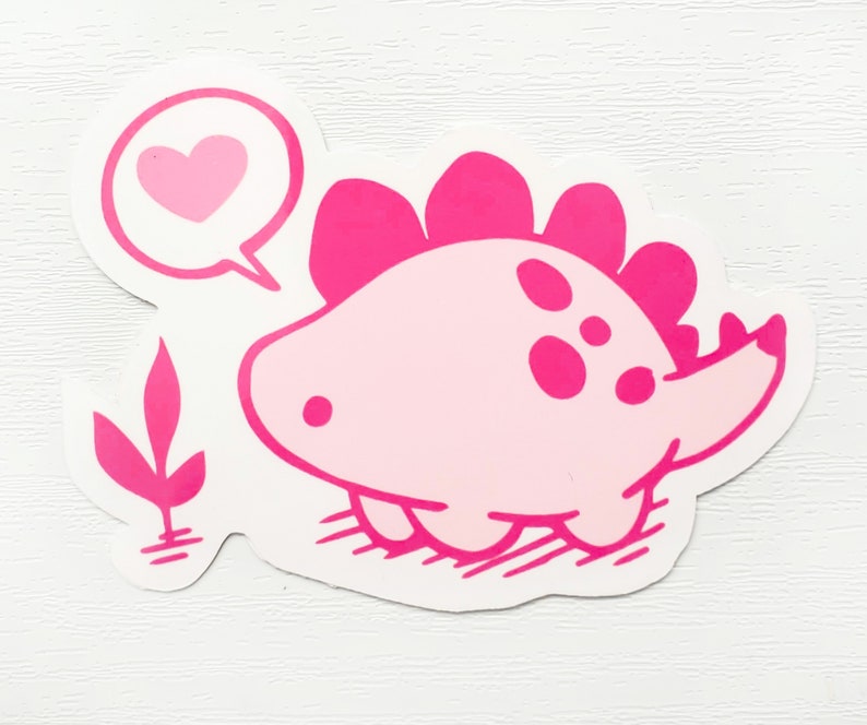 May include: A pink dinosaur sticker with a speech bubble containing a pink heart. The dinosaur has a light pink body, darker pink spines, and a small tail. A pink plant is next to the dinosaur.