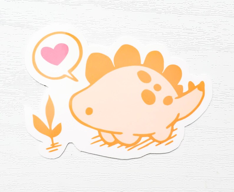 May include: A sticker featuring a cartoon dinosaur in shades of orange and peach. The dinosaur has a speech bubble with a pink heart. The sticker has a white border and a small orange plant graphic.