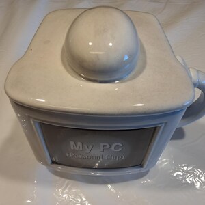 May include: A light gray ceramic mug with a matching lid featuring a rounded top knob. The front of the mug displays a rectangular inset panel with the text "My PC (Personal Cup)" printed in white. The mug includes a curved handle on the side.