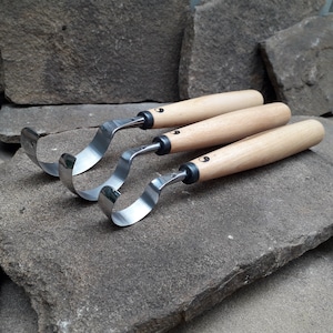 May include: Three wood carving tools with curved blades and wooden handles. The tools are arranged in a stack, with the largest tool on the bottom and the smallest tool on top. The tools are made of metal and wood and have a natural finish.
