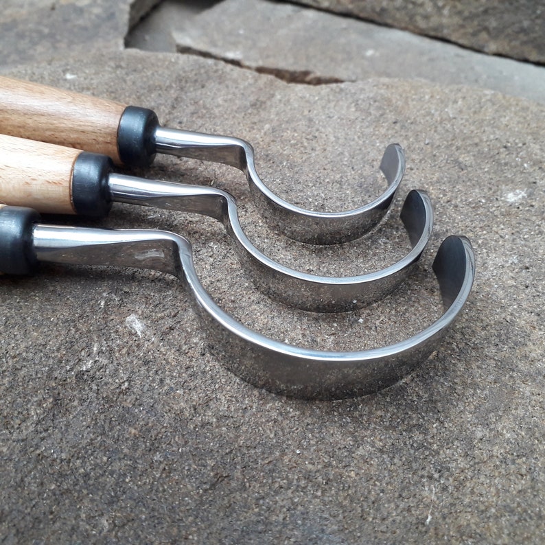 May include: Three wood carving tools with curved blades and wooden handles. The tools are arranged in a stack, with the largest tool at the bottom and the smallest tool at the top.