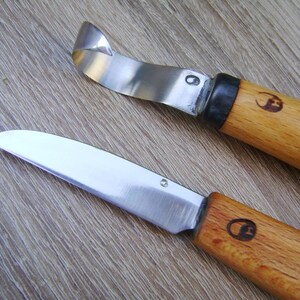 Op de afbeelding: Twee snijmesjes met houten handvatten en zilveren messen. Het mes aan de linkerkant heeft een gebogen mes en het mes aan de rechterkant heeft een recht mes.